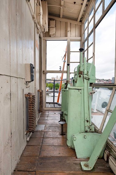 A photograph of the inside of the cab of a 20th century dockside crane, with an array of levers. Through the window there is a view of Bristol city centre. 