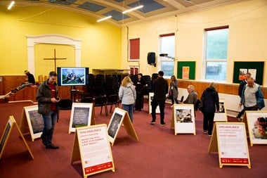 People perusing images displayed on A-frame boards in a church hall.
