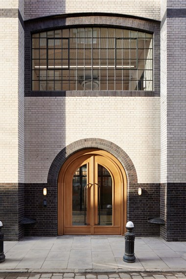 A square-on photo of the wooden doorway to a white and black brick office building. A large, latticed window is above the doorway on the first floor.