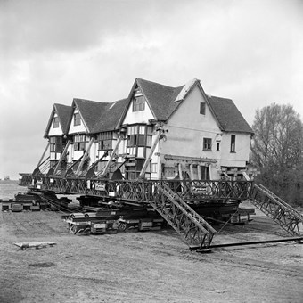 Archive photograph of a timber framed house lifted on ramps and trolleys.