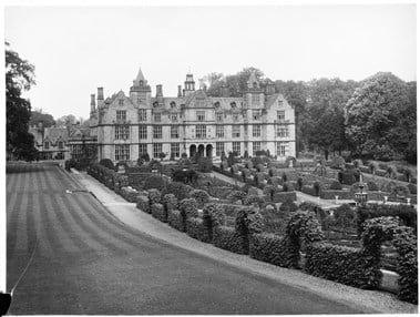 archive black and white photograph of a large country house with formal gardens in the foreground