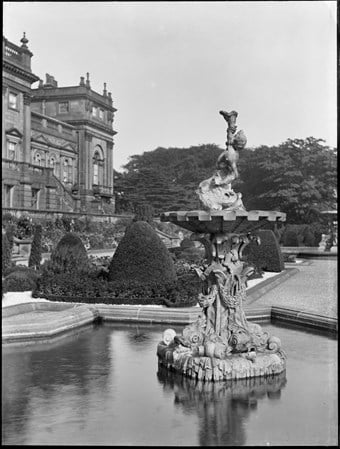 archive black and white photograph of a fountain surmounted by a figure in the formal gardens of a large country house