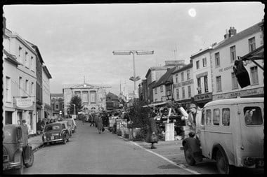 archive black and white photograph of a busy street scene with people and vehicles