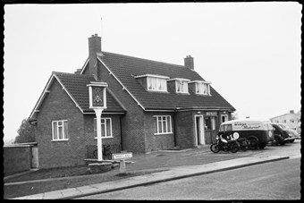 archive black and white photograph of a building with vehicles parked and a sign