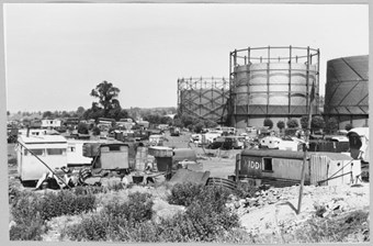 archive black and white photograph of three gasholders with caravans in the foreground