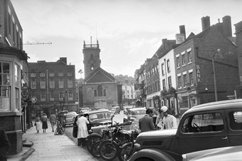 archive black and white photograph of  a busy street scene with people and vehicles