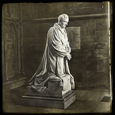 Archive photo showing a stone monument of a kneeling man in long robes.