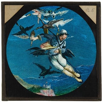 A hand-coloured decorative slide showing an engraving of a man held aloft by ducks. He is seen flying above a cliff-top castle.