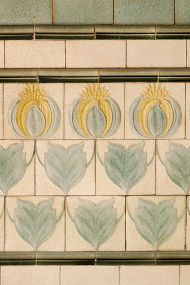 Glazed tiles featuring repeated green and yellow motif of a flower and foliage on a cream background.