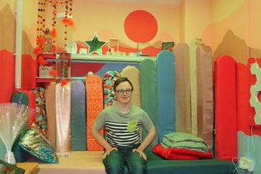 Portrait of a young man sitting in a colourfully decorated and upholstered room. 