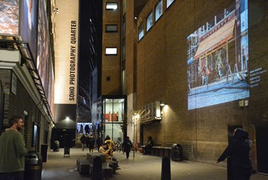 Image being projected onto a wall with people walking passed.