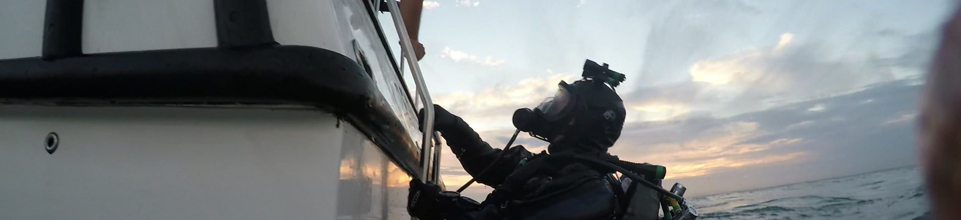A diver wearing SCUBA equipment prepares to climb up a ladder from a boat following a dive.