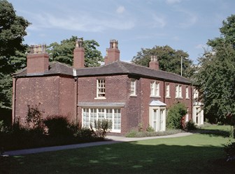 Colour photo of large red brick house surrounded by lawns and large trees.