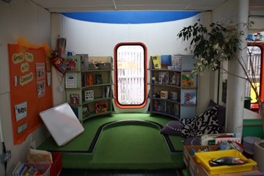 Interior photo of a primary school classroom with a primary green coloured carpet, a blue framed rounded rectangular window