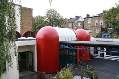  Exterior photo of a school courtyard dominated by a primary red domed pod-like entrance
