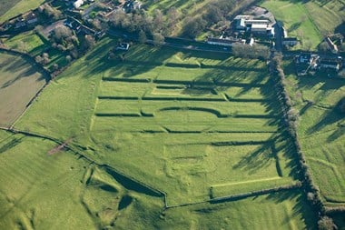 Colour aerial photo showing a series of terraces with other hollows and banks in pasture fields with village houses beyond