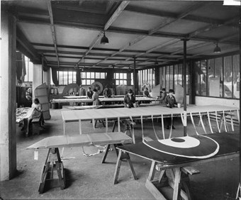 Waring and Gillow’s factory and depository, Hammersmith, London, November 1916 Women applying dope to stiffen the fabric of bi-plane wings. The roundel of the Royal Flying Corps is in the foreground. (BL23701/011)