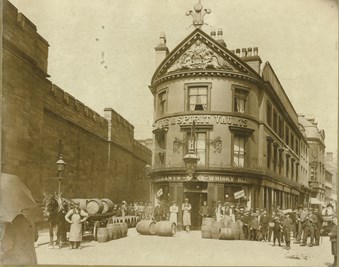 Exterior view of The Spirit Vaults public house with barrels being offloaded from a horse-drawn wagon in front.