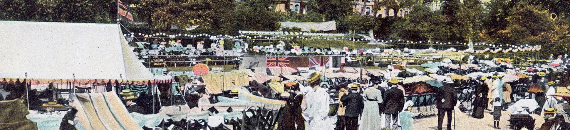 Victorian postcard of visitors sat in rows of deck chairs at Alexandra Park, with houses visible in the background through the trees
