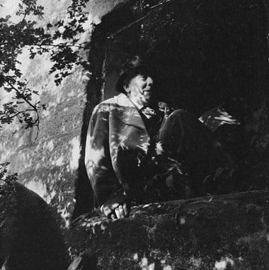 A man seated in the window opening of a derelict watermill