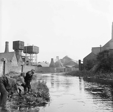Three boys on the bank of the Caldon Canal with the kilns of Joiners Square Mill in the background