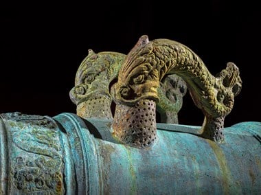 Two dolphin-shaped handles rise from the barrel of a bronze cannon.