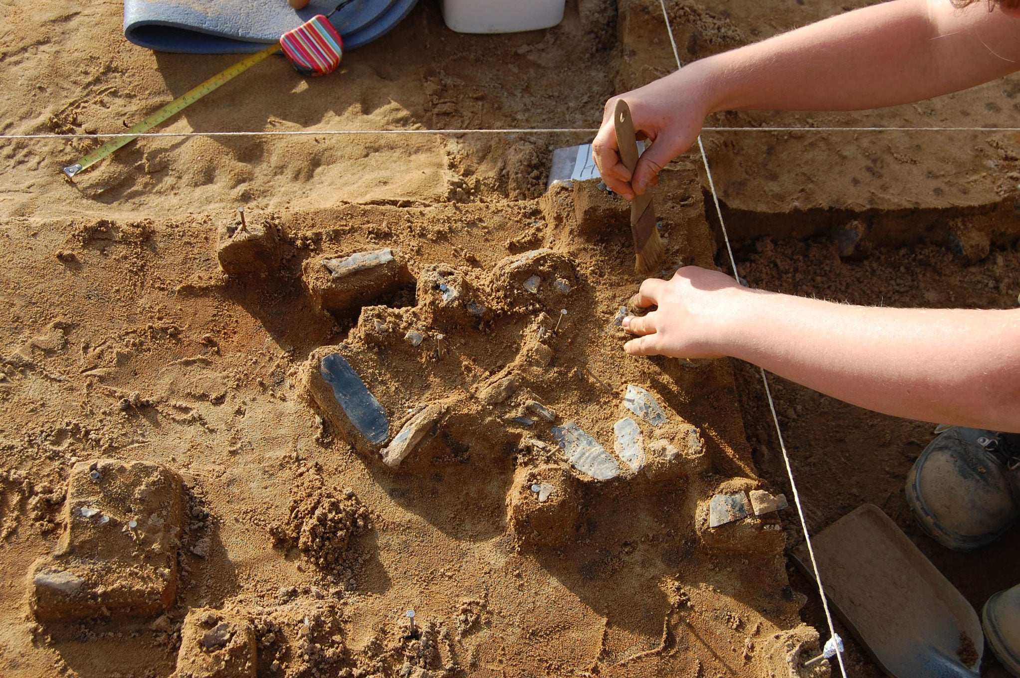 A detail of an archaeologist excavating flint tools at a sight marked off into a grid by strings.
