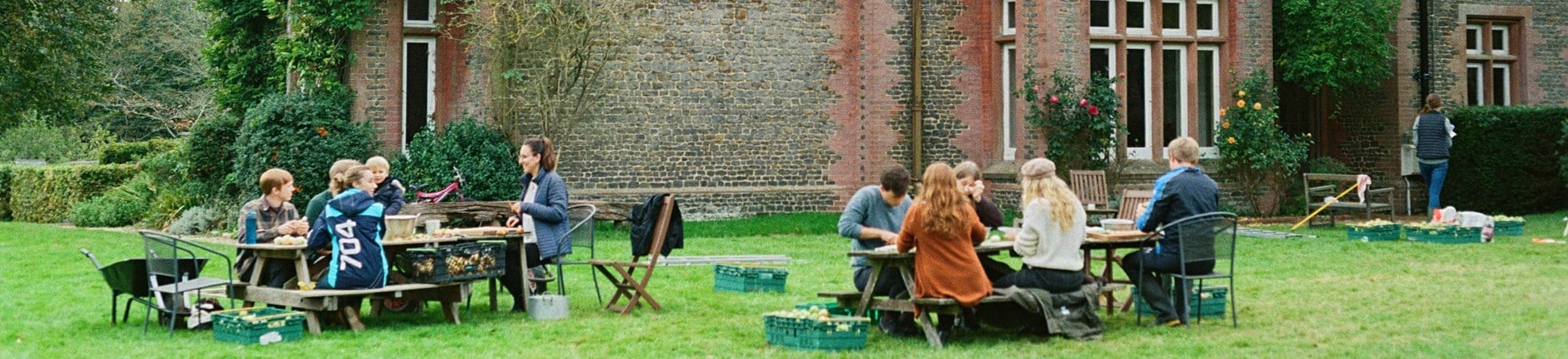 People sat on picnic benches outside a historic house.