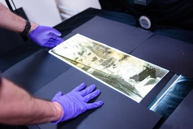 Gloved hands of a staff member at the Historic England Archive. The hands carefully position the negative on a copy stand prior to digital capture. 