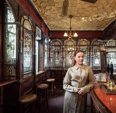 Manager of a pub leaning against the bar with decorative etched glass mirrors along two walls.