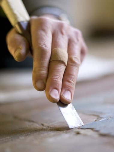 Image of someone scraping residue off historic tiles using a chisel.