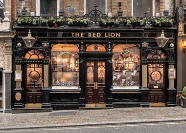 Exterior view of The Red Lion pub with three doorways and windows all with ornate etched glass.