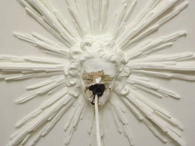 Damaged ceiling decoration of a head with an electric cable running through a hole in the face.