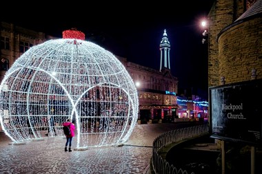 A night time scene showing a giant bauble illuminated with Christmas lights on St John's Square