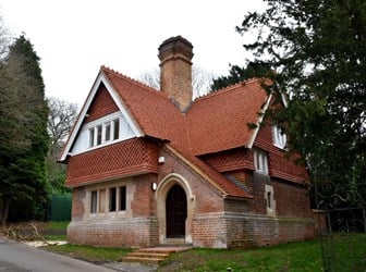Red brick building with central chimney and tiled steeply sloped roof.