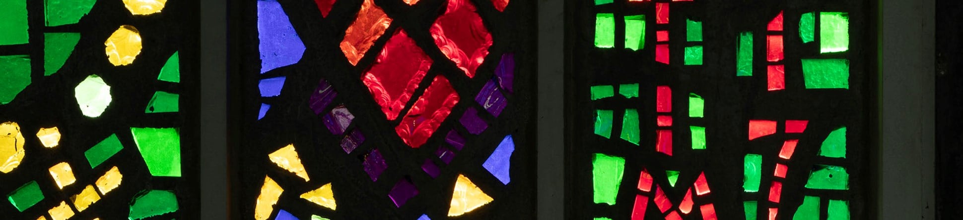 The photo shows three panels of chunky glass design, with vibrant red, green, yellow and blue in a black background, with a heart in the centre panel.