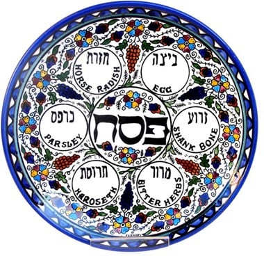A plate decorated with floral patterns and inscriptions of ingredients in Hebrew and English: clockwise these read horse radish, egg, shank bone, bitter herbs, haroseth (haroset) and parsley.