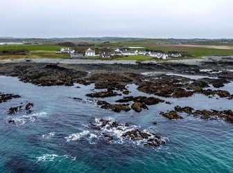 Photo looking inland with the sea lapping a rocky shore and a village close to the coastline.