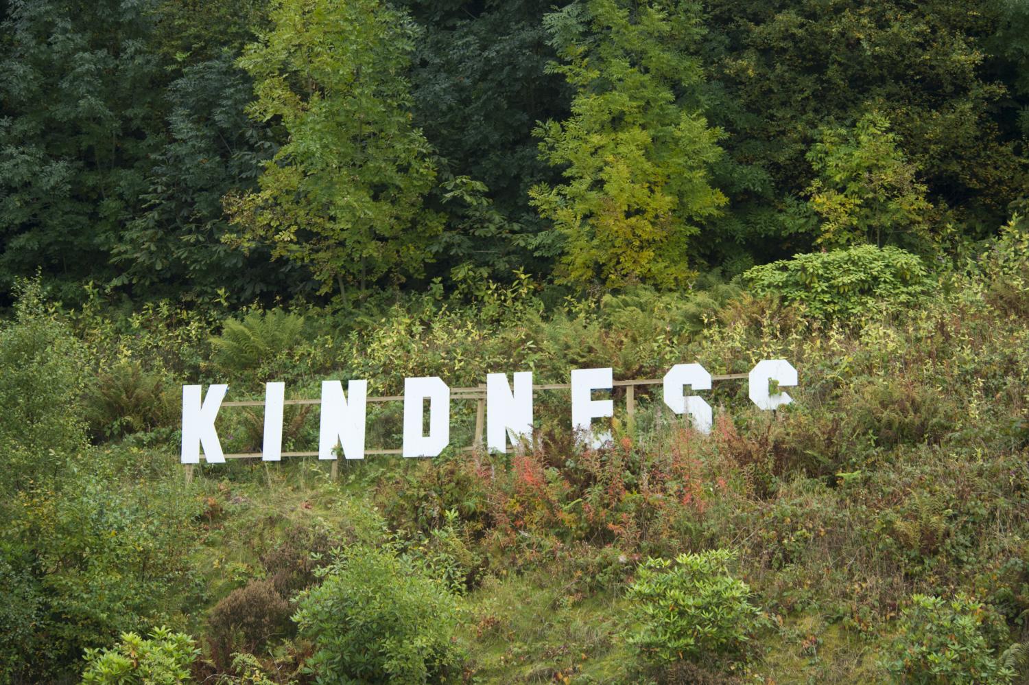 A white logo spelling K-I-N-D-N-E-S-S on a hillside in the style of the Hollywood signage.
