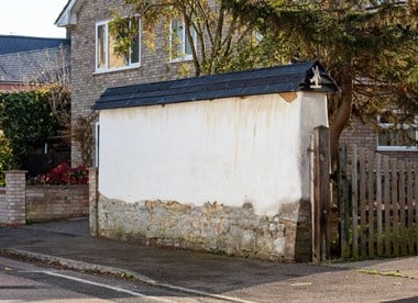 Wall with stone base and render upper section in front of a house.