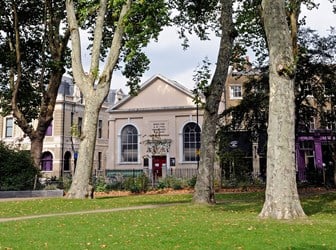 A low chapel building sits on the edge of a London park, with townhouses on each side.