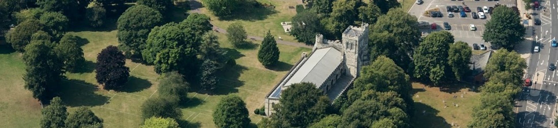 The Priory Church of St Peter is shown in an aerial view, surrounded by trees and with the landscaped Priory grounds around it.