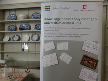 A vertical banner bearing the message "Knowledge doesn't belong to universities or museums" The banner invites participants to share their discovery stories, examples are written on cards pinned to the banner.