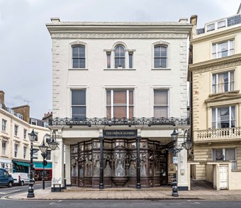 Period building with etched glass windows of the Prince Alfred pub on ground floor level and cast-iron lamp standards outside on the pavement.