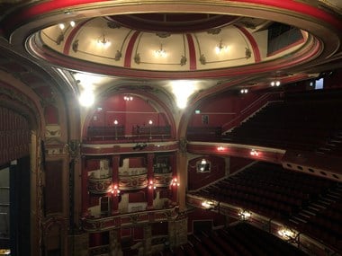 The decorated domed ceiling, seating and balconies of a theatre interior.