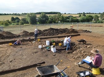 A team of people working on an archaeological site, excavating and recording features.