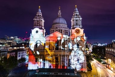 Images of members of the St Paul's Watch are projected on the west elevation of St Paul's Cathedral. One of them holds a fire hose.