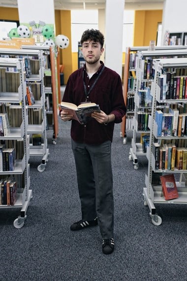Portrait of a library assistant posed for the camera with an open book, at Prescot Library