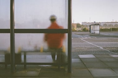 A view from behind showing a person wearing a bike helmet, sitting at a bus stop