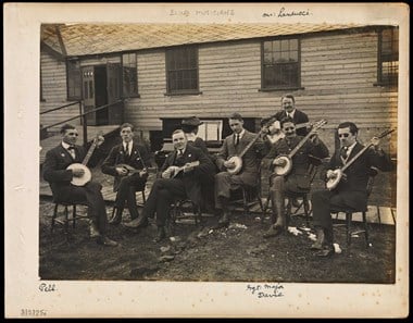 A band of seven blinded veterans seated playing the banjo.